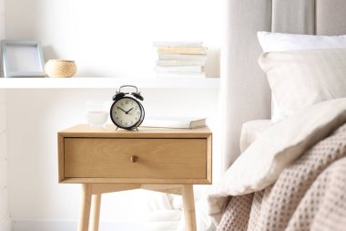 Alarmlı komodinli komodin, bir bardak su ve yatağın yanında kitap.