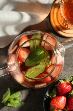 Gri masada aromatik meyve çayı, çilek ve nane aromalı cam çaydanlık.