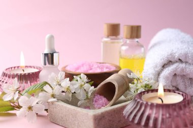 Kozmetik ürünleriyle spa kompozisyonu, yanan mumlar ve pembe arka planda güzel çiçekler, yakın plan.