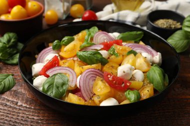 Sarı domatesli lezzetli salata, fesleğen, soğan ve ahşap masada mozzarella peyniri, yakın plan.