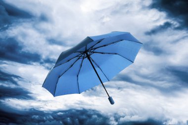 Bulutlu gökyüzünde uçan mavi şemsiye. Fırtınalı hava