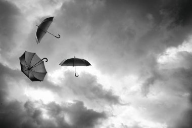 Bulutlu gökyüzünde uçan siyah şemsiyeler. Fırtınalı hava