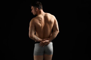 Siyah arka planda açık gri iç çamaşırlı genç adam.