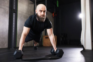 Sporcu spor salonunda halterli şınav çekiyor.