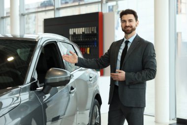 Salondaki yeni gri arabanın yanındaki mutlu satıcı.