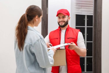 Kutu ve alıcıyla gülümseyen kurye paket teslimatı için imza atıyor.