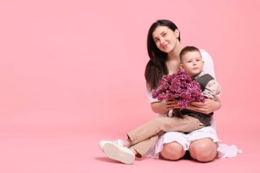 Anne ve oğlu pembe arka planda bir buket leylak çiçeğiyle, mesaj atmak için yer var.