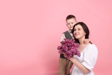 Anne ve oğlu pembe arka planda bir buket leylak çiçeğiyle, mesaj atmak için yer var.