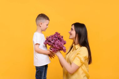 Anne ve oğlu sarı arka planda bir demet leylak çiçeğiyle