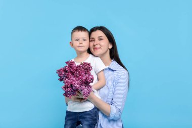 Anne ve oğlu açık mavi arka planda bir demet leylak çiçeğiyle