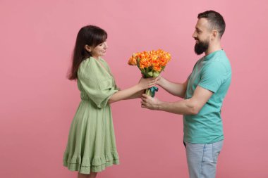 Adam pembe arka planda sevgili karısına bir buket güzel lale sunuyor.