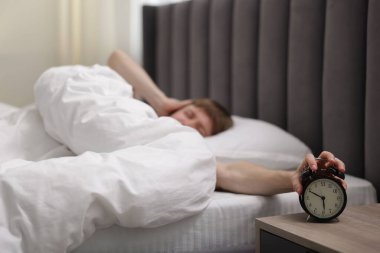 Yataktaki çalar saati kapatan uykucu adam, seçici odaklanma