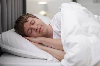 Genç adam yatağında uyuyor.