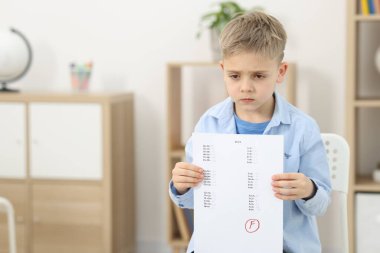 Okul derecesi. Cevap kağıdını tutan üzgün çocuk. Kapalı alanda F harfi, mesaj için boşluk.