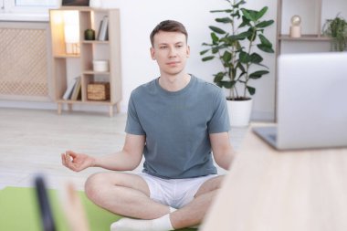 Evde bilgisayarla yoga dersi alan bir adam.