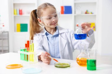 Küçük kız içeride masada kimyasal deney yapıyor.