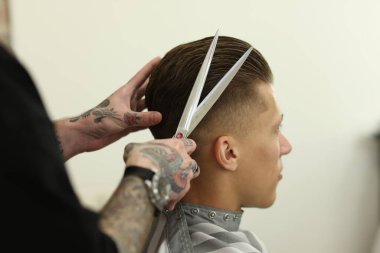 Profesyonel berber, berber dükkanında müşterinin saçını makasla kesiyor.