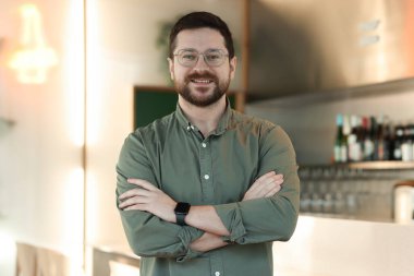 Kafesinde kollarını kavuşturmuş gülümseyen bir işadamının portresi.