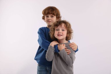 Beyaz arka planda kucaklaşan sevimli küçük kardeşler.