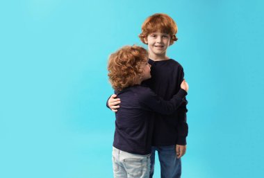 Açık mavi arka planda kucaklaşan sevimli küçük kardeşler. Metin için boşluk