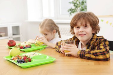 Okuldaki ahşap masada yemek yiyen şirin küçük çocuklar.