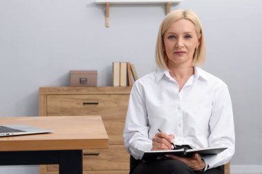 Profesyonel psikolog ofisteki masanın yanında notlar alıyor.