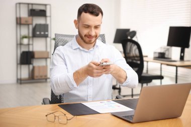 Ofisteki masada akıllı telefondaki tarama uygulamasını kullanarak belgenin fotoğrafını çeken bir adam.