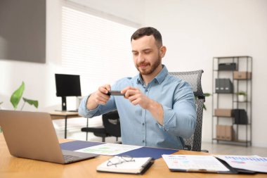 Ofisteki masada akıllı telefondaki tarama uygulamasını kullanarak belgenin fotoğrafını çeken bir adam.