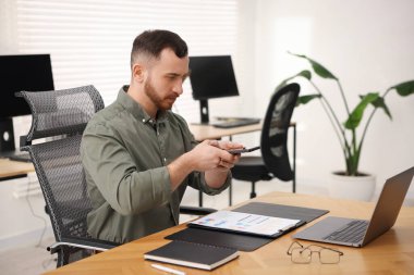 Ofisteki masada akıllı telefondaki tarama uygulamasını kullanarak belgenin fotoğrafını çeken bir adam.