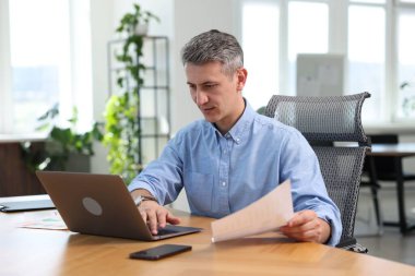 Ofiste evrak ve dizüstü bilgisayarla çalışan bir işadamı.