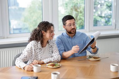 İş arkadaşları yemek yiyor ve ofiste öğle arasında iş tartışıyorlar.