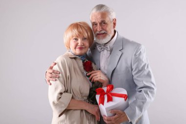 Hediye kutusu olan ve açık gri arka planda gül gülü olan sevimli yaşlı çift.