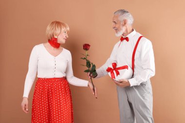 Hediye kutusu olan ve açık kahverengi arka planda gül gülü olan sevimli son sınıf çifti