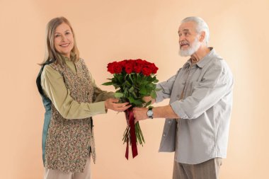 Adam bej arka planda mutlu karısına kırmızı güller sunuyor.