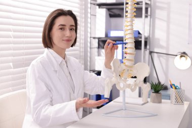 Doktor, klinikteki masadaki insan omurga modeline işaret ediyor.