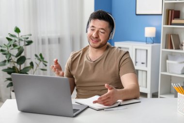 İçerideki masada dizüstü bilgisayarla öğretmenle online ders alan bir adam.