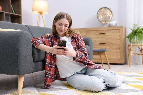Улыбающаяся девочка-подросток со смартфоном на полу дома