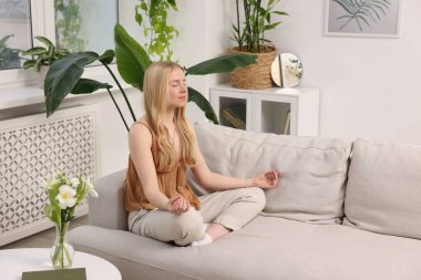 Feng shui. Evdeki kanepede meditasyon yapan genç bir kadın.