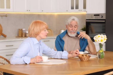 Mutfaktaki ahşap masada birlikte kahvaltı eden sevimli yaşlı çift.