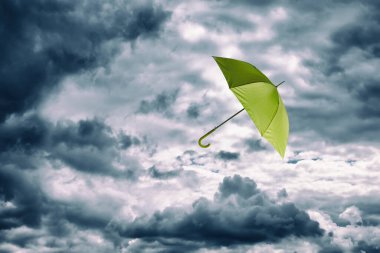 Açık yeşil şemsiye bulutlu gökyüzünde uçuyor. Fırtınalı hava