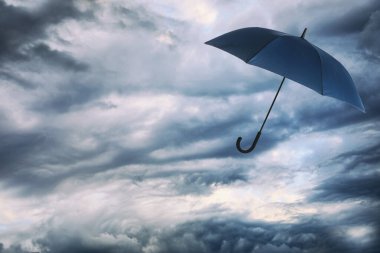 Bulutlu gökyüzünde uçan koyu mavi şemsiye. Fırtınalı hava