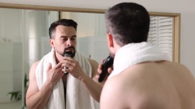 Yakışıklı adam banyoda aynanın yanında tıraş makinesiyle tıraş oluyor.