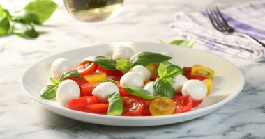 Beyaz mermer masada peynirli, domatesli ve fesleğenli salataya yağ ekleyen kadın, yakın plan.