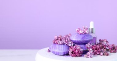 Beyaz masada pembe arka planda sabun, deniz tuzu, esaslı yağ ve leylak çiçekli yuvarlanan podyum, yakın plan. Metin için boşluk