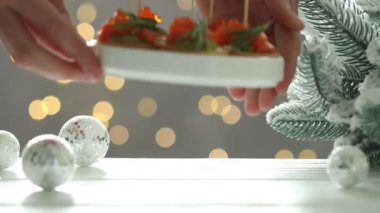 Beyaz ahşap masaya, arka planda bulanık ışıkları olan, nefis kanepeler koyan bir kadın. Bokeh etkisi