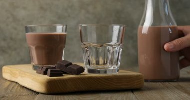 Ahşap masada lezzetli çikolatalı sütü bardağa dolduran kadın, yakın plan.