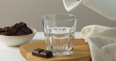 Beyaz ahşap masada lezzetli çikolatalı sütü bardağa dolduran kadın.