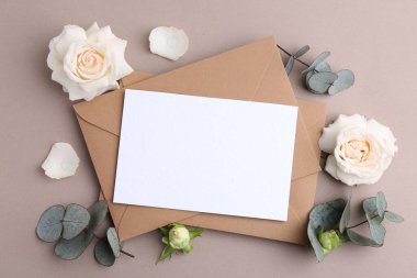 Boş tebrik kartı, kağıt zarflar, gül çiçekleri ve bej arka planda okaliptüs dalları, düz uzanma