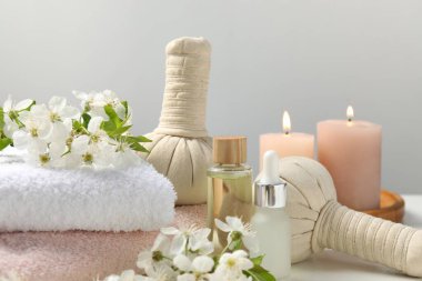 Gri arka plan ve yakın plan karşısında beyaz masadaki güzel çiçeklerle kaplıca ürünleri ve dallar