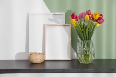 Renkli duvarın yanındaki masada bir buket güzel lale ve çerçeveler.